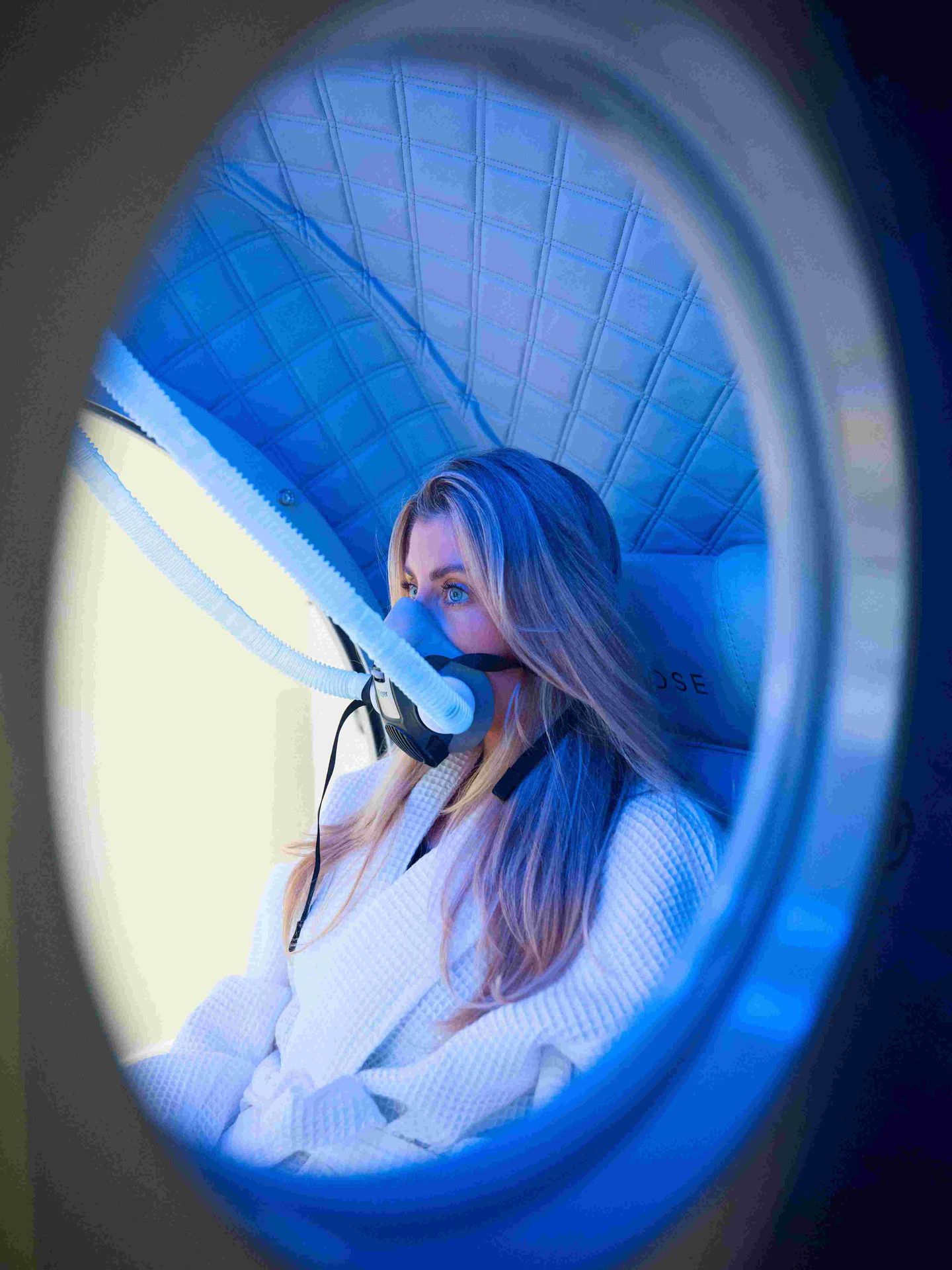 Woman experiencing an advanced biohacking chamber with illuminated blue lighting and specialized wellness technology.